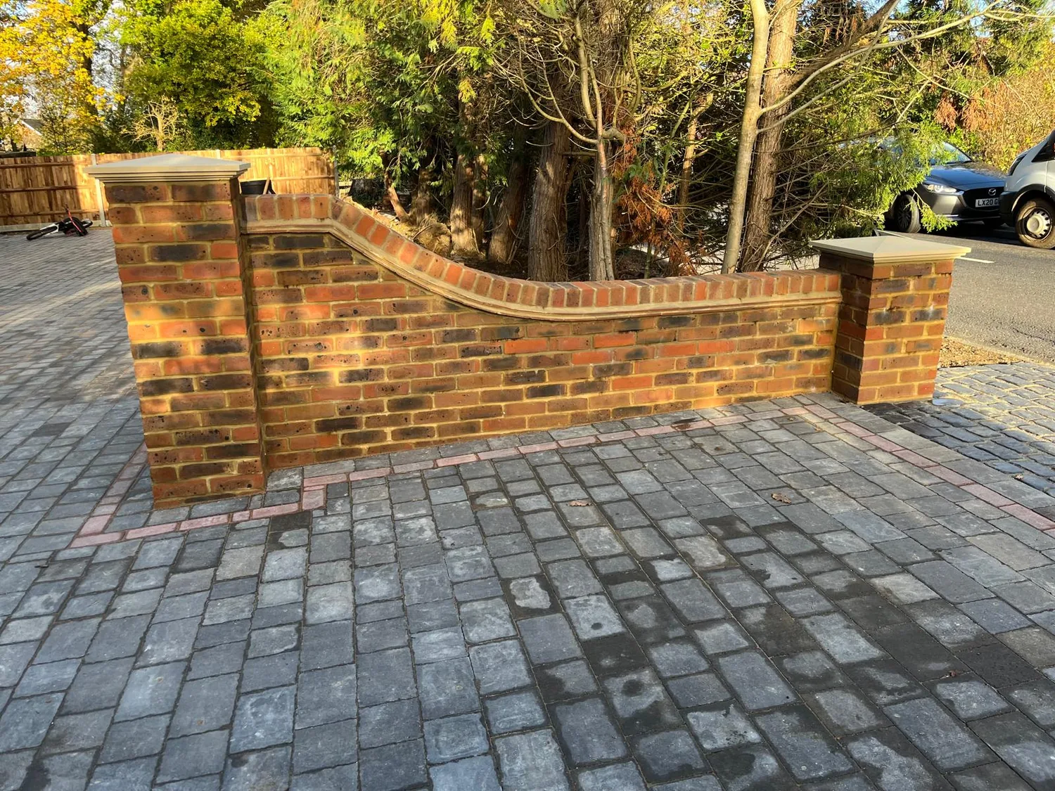 Curved brick garden wall with rounded coping running beside a block paved drive