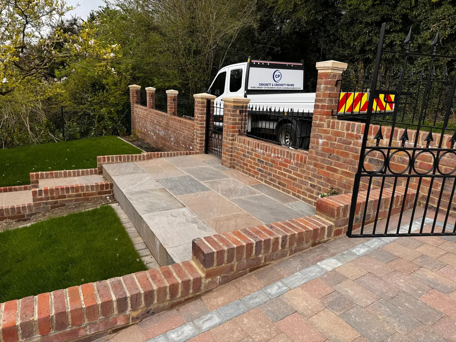 Brick piers and a wall with iron railings, and the company tipper on the drive behind