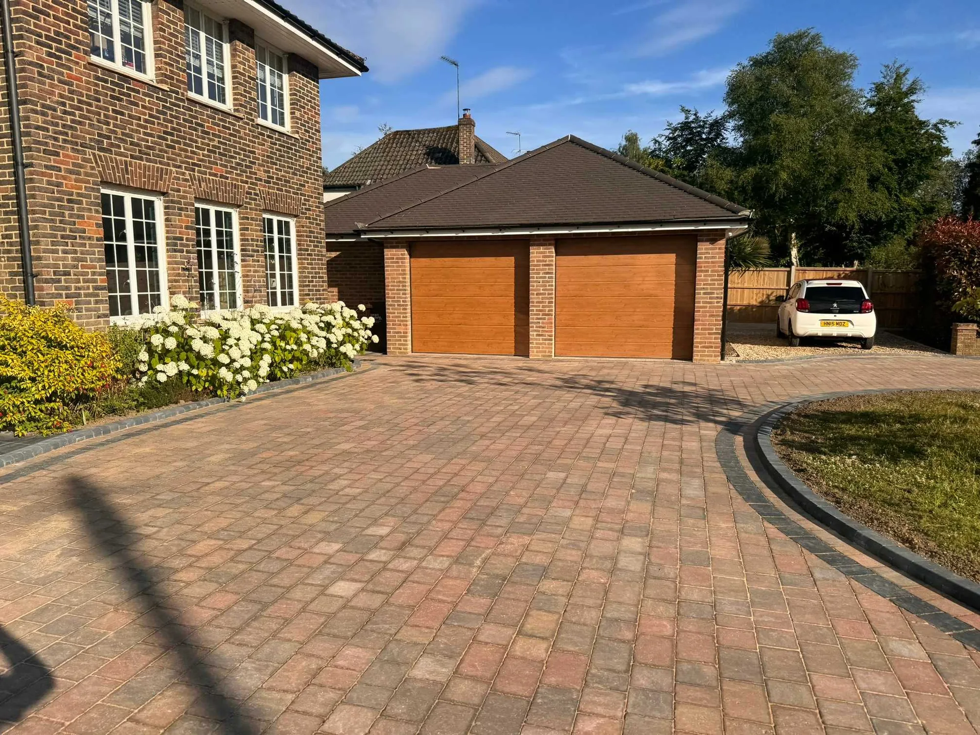 Curved block paved driveway running up to a double garage at a brick house