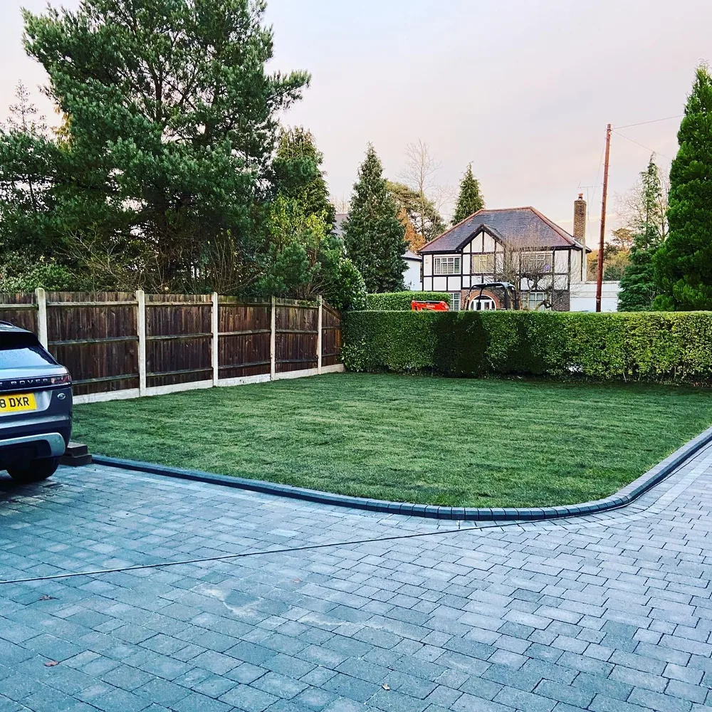 Blue grey block paved driveway laid to a new lawn behind a close boarded fence