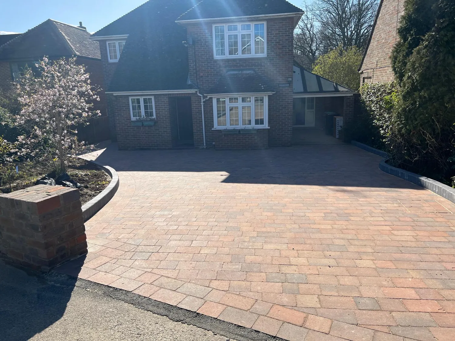 Brindle block paved driveway curving up to a detached house behind a brick retaining wall