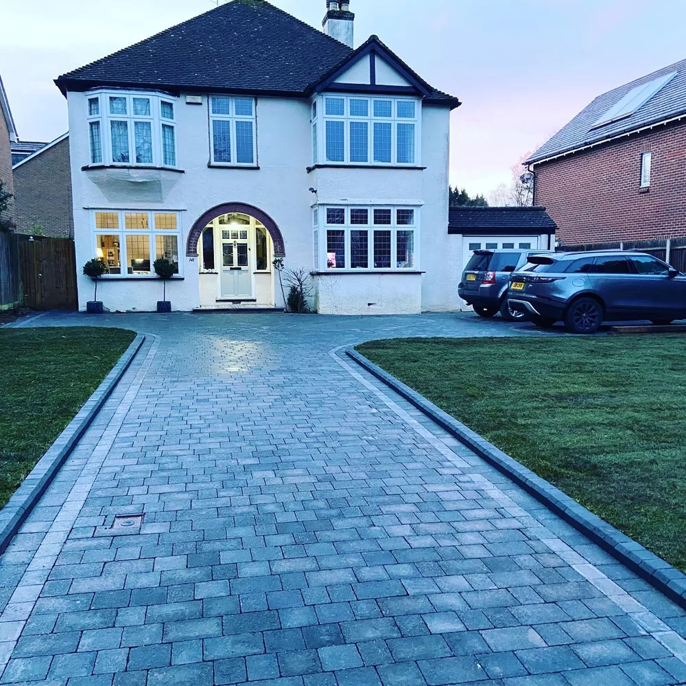 Blue grey block paved driveway laid to a 1930s detached house at dusk