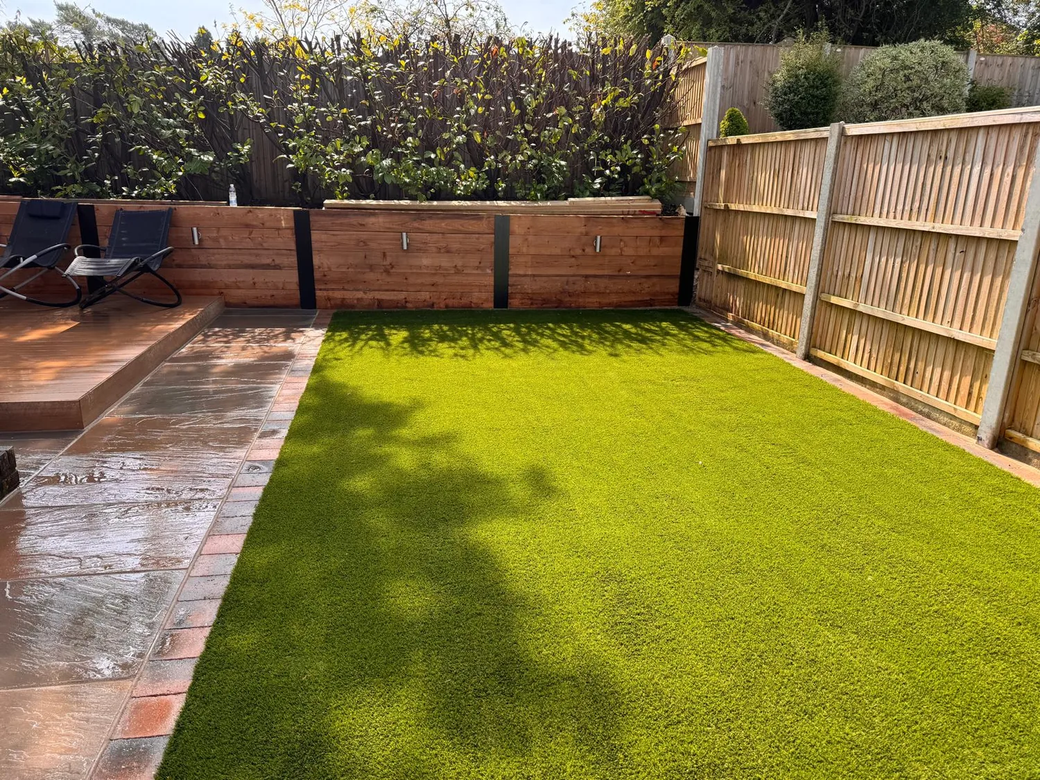 Artificial lawn edged with sleepers and a paved border in an enclosed rear garden