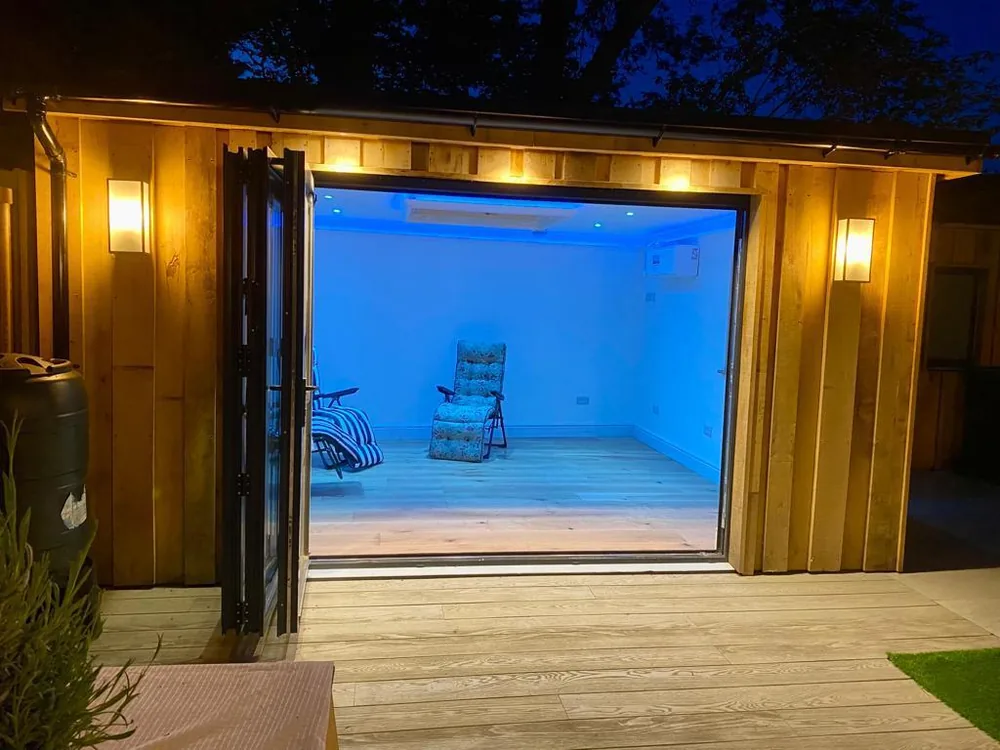 Timber garden room lit at dusk with the bi-fold doors open