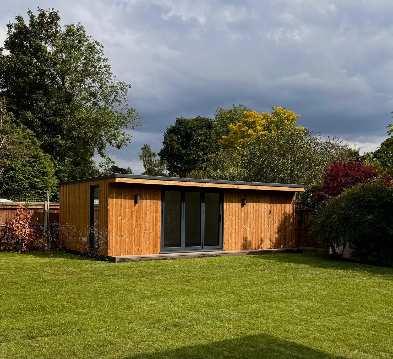 Large larch clad garden room with bi-fold doors on a new lawn under a dramatic sky