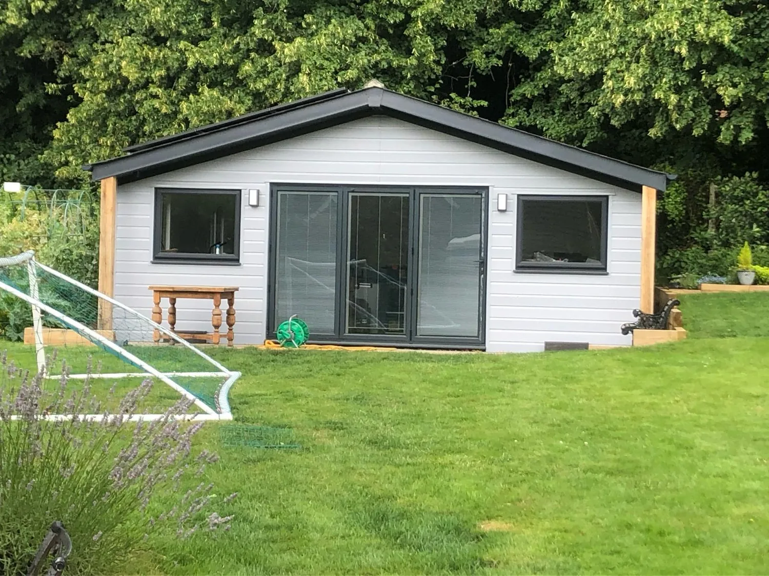 Modern white and timber garden room set on a lawn behind a large house