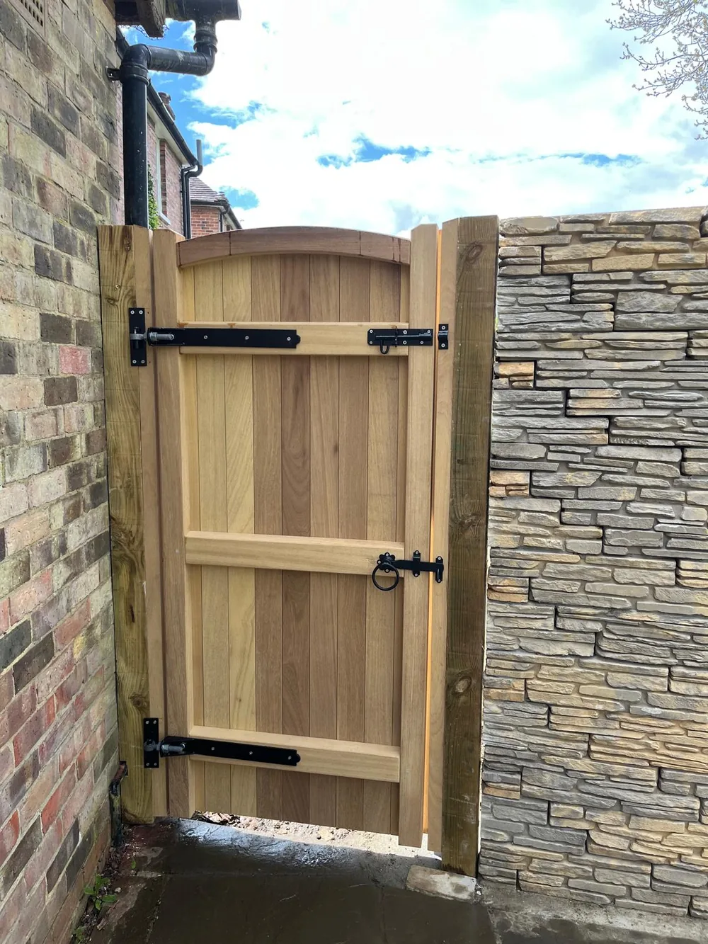 Timber side gate hung between a stone clad pier and a rendered wall