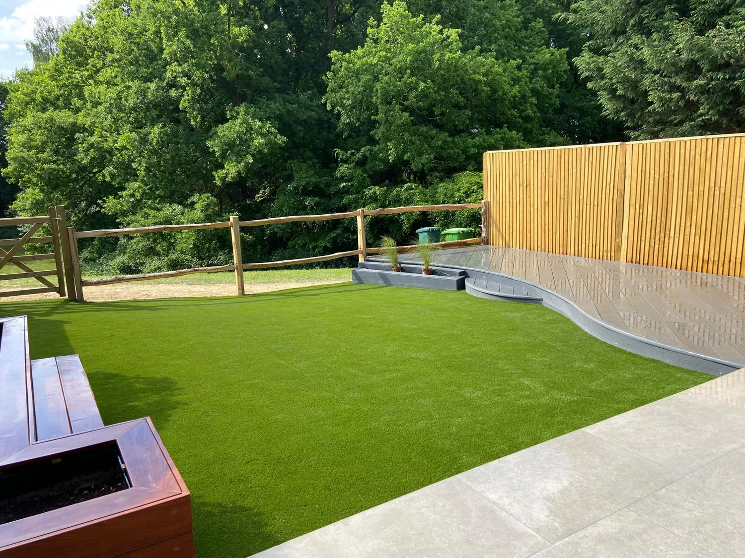 Artificial lawn edged with sleepers against a close boarded fence