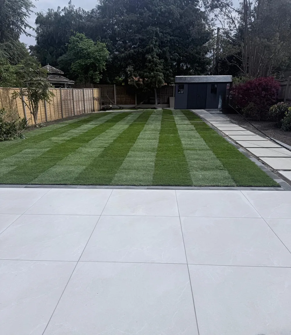 Freshly laid striped lawn beside a porcelain patio, with a garden building at the far end