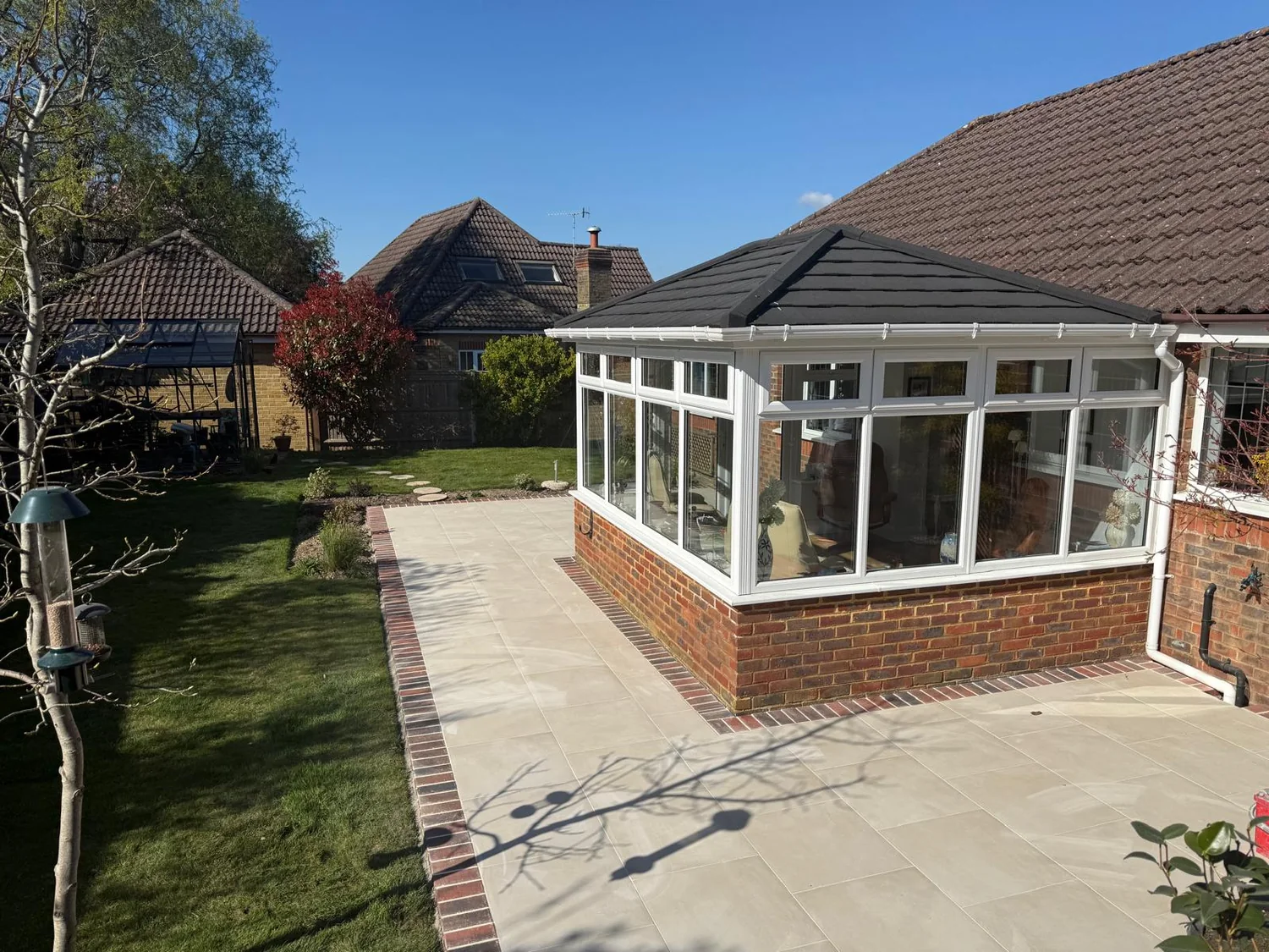 Sandstone patio with a brick edge wrapping around a conservatory beside the lawn