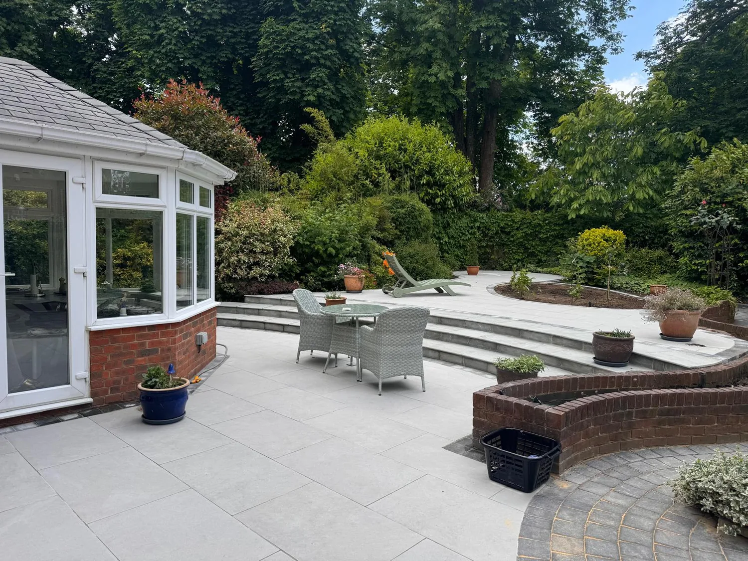 Large porcelain patio with curved brick raised beds beside a conservatory