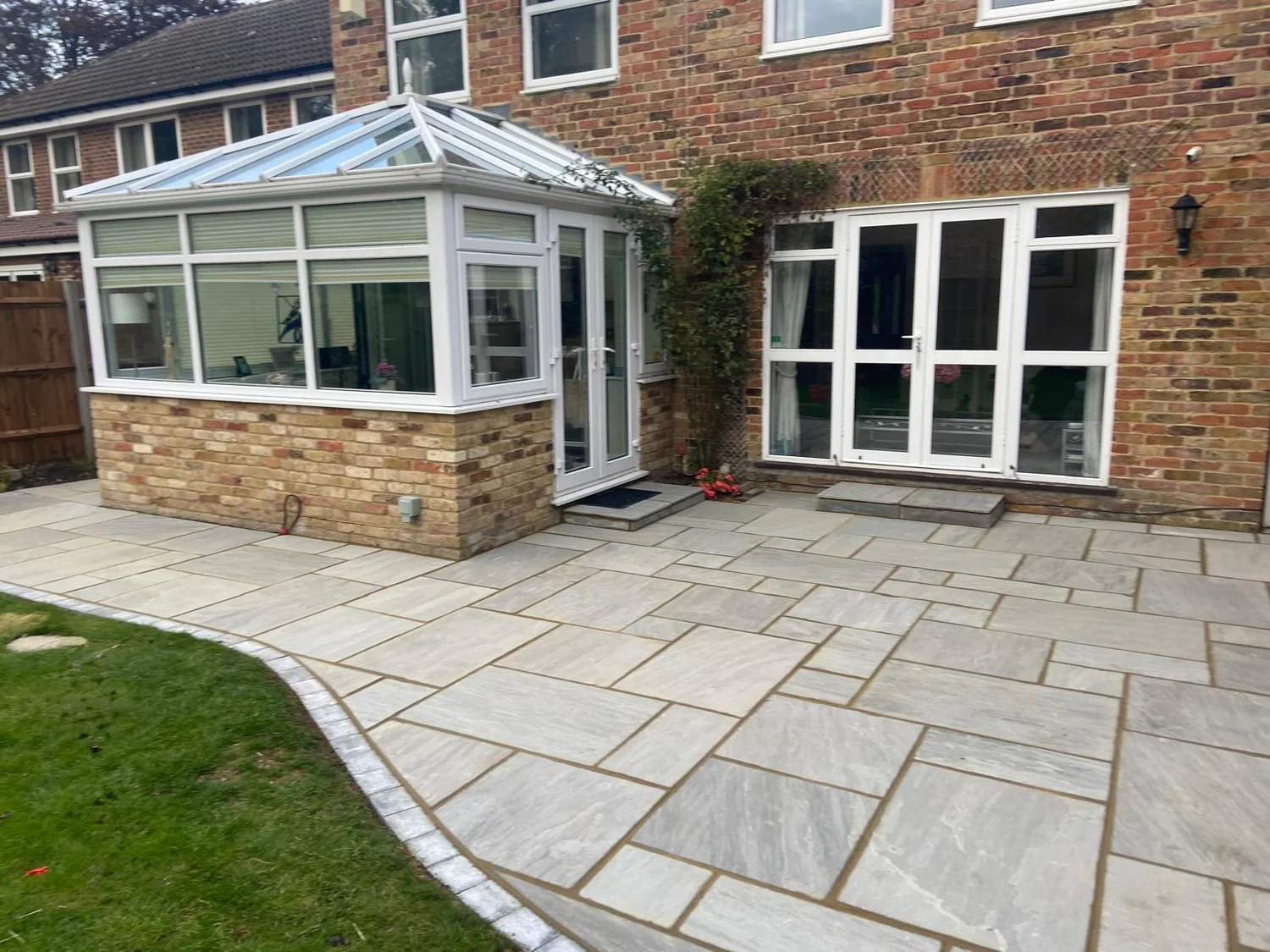 Grey sandstone patio with a curved edge to the lawn outside an orangery