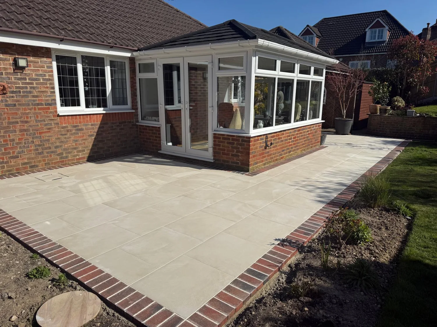 Porcelain patio with a brick border wrapping around the conservatory of a bungalow