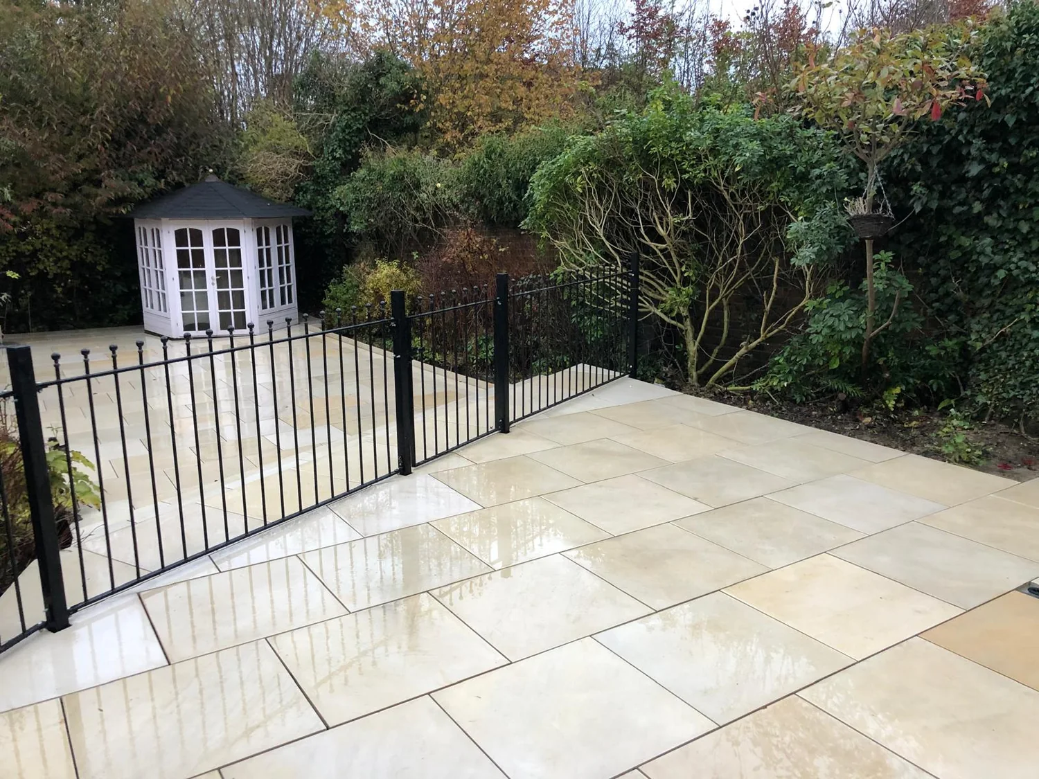 Sandstone patio with black metal railings and a summer house in the corner of the garden
