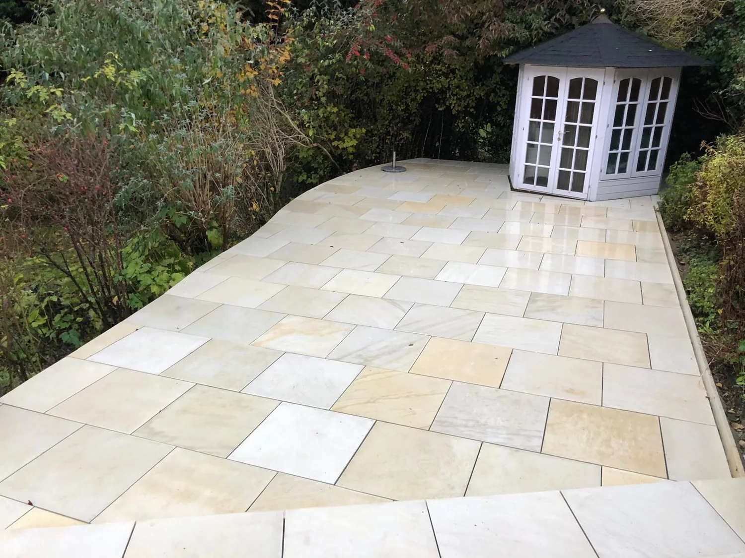 Large sandstone patio laid up to a painted summer house in a wooded garden