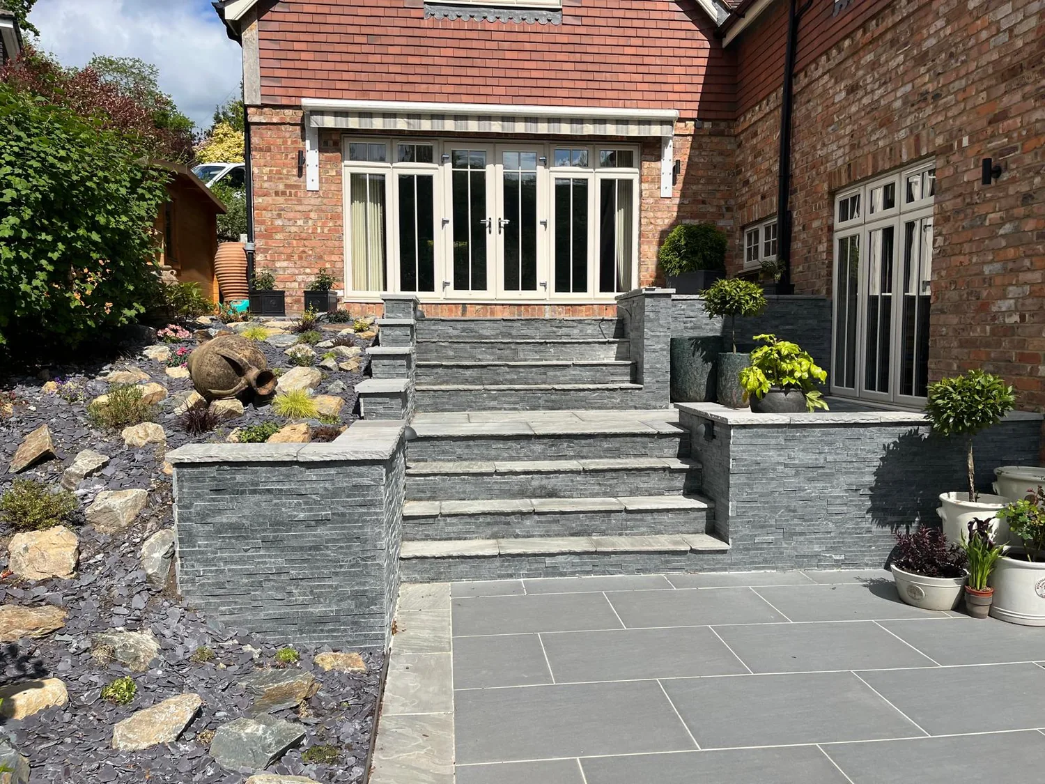 Slate patio with steps and a rockery running up to a brick house