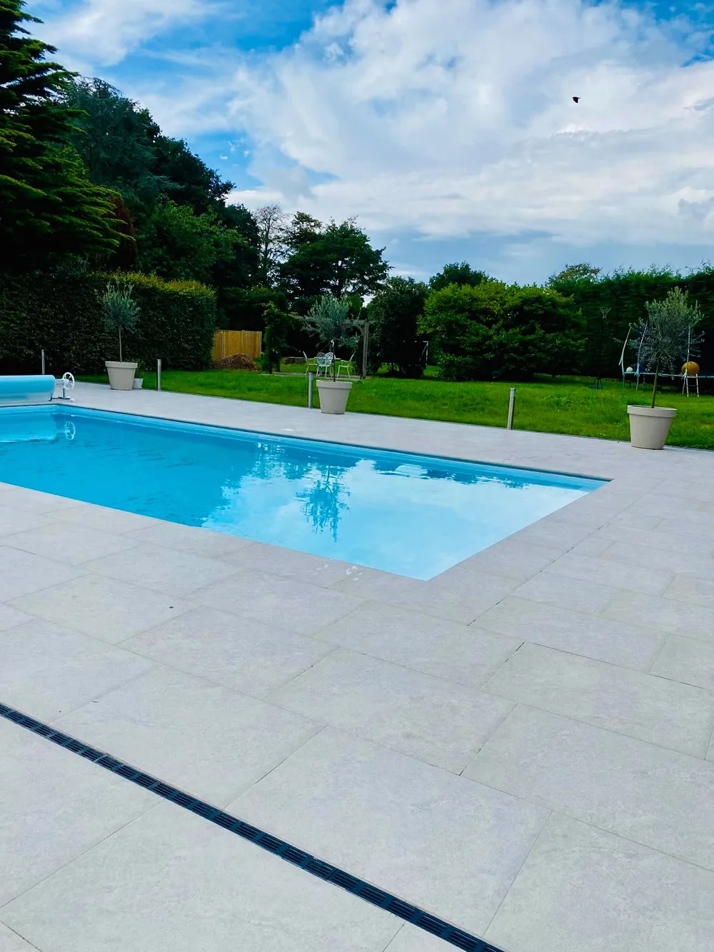 Porcelain paving laid around a swimming pool with the lawn and mature trees beyond