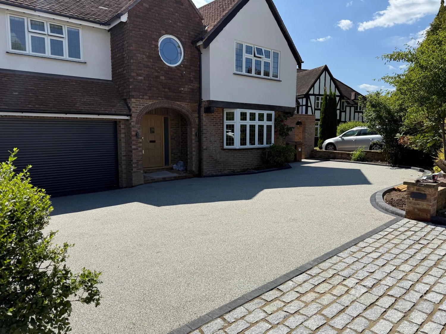 Silver grey resin-bound driveway with a granite sett apron in front of a detached house