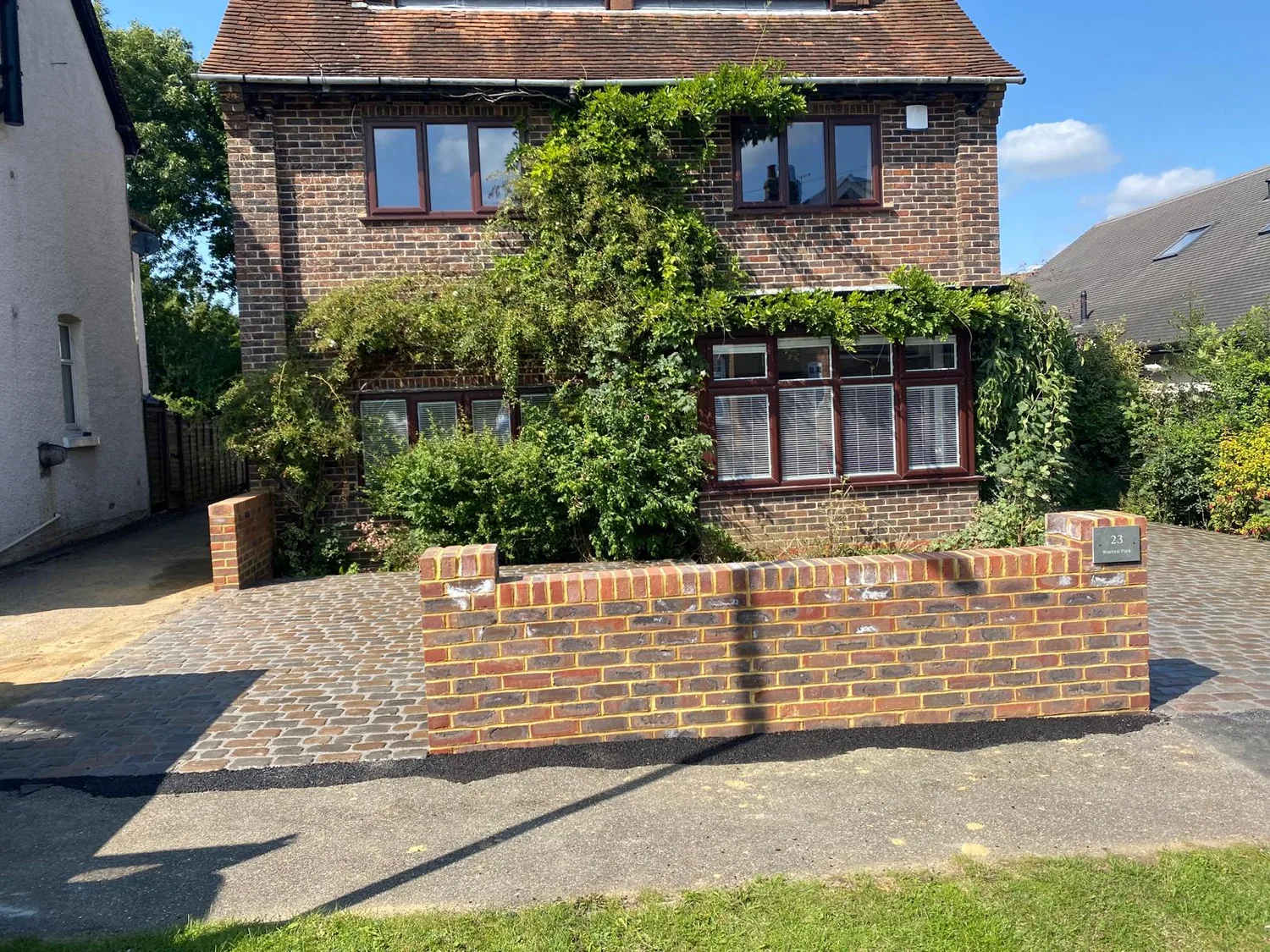 Brick retaining wall holding a raised lawn above a block paved drive