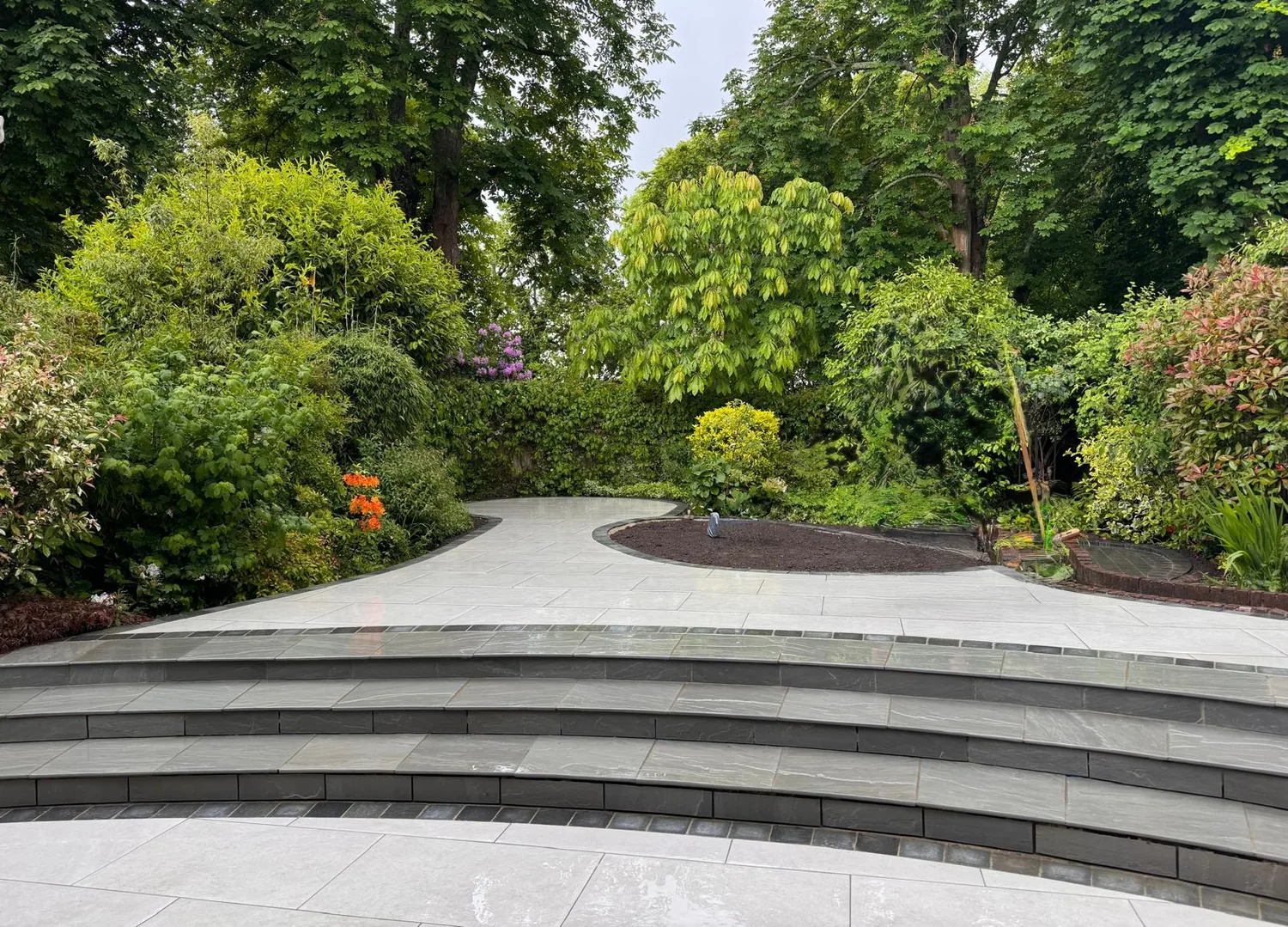 Porcelain terrace with sweeping curved steps rising into a mature planted garden