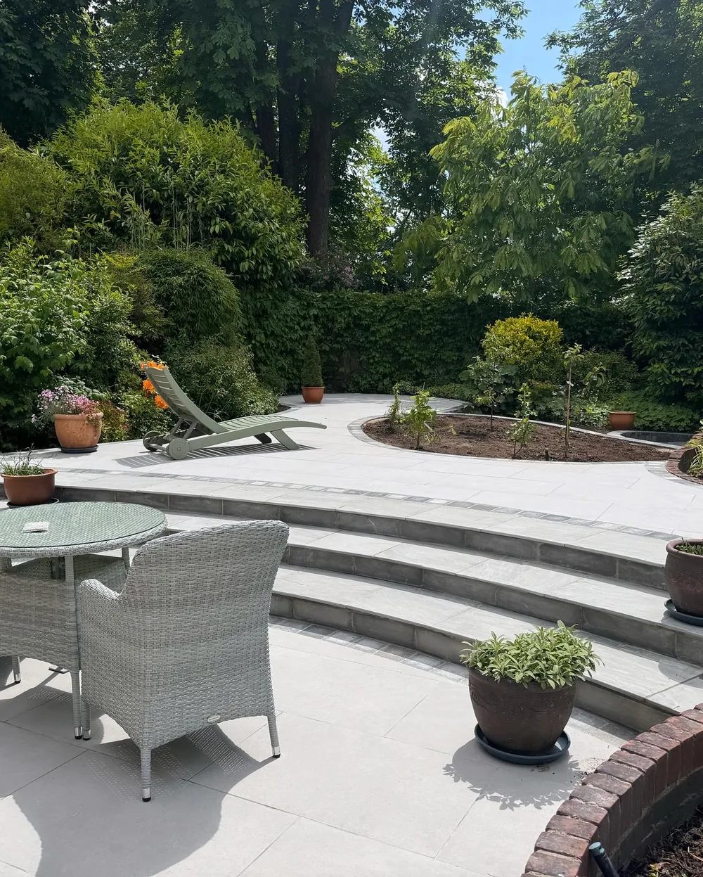 Curved porcelain terrace with sweeping steps rising into a mature planted garden