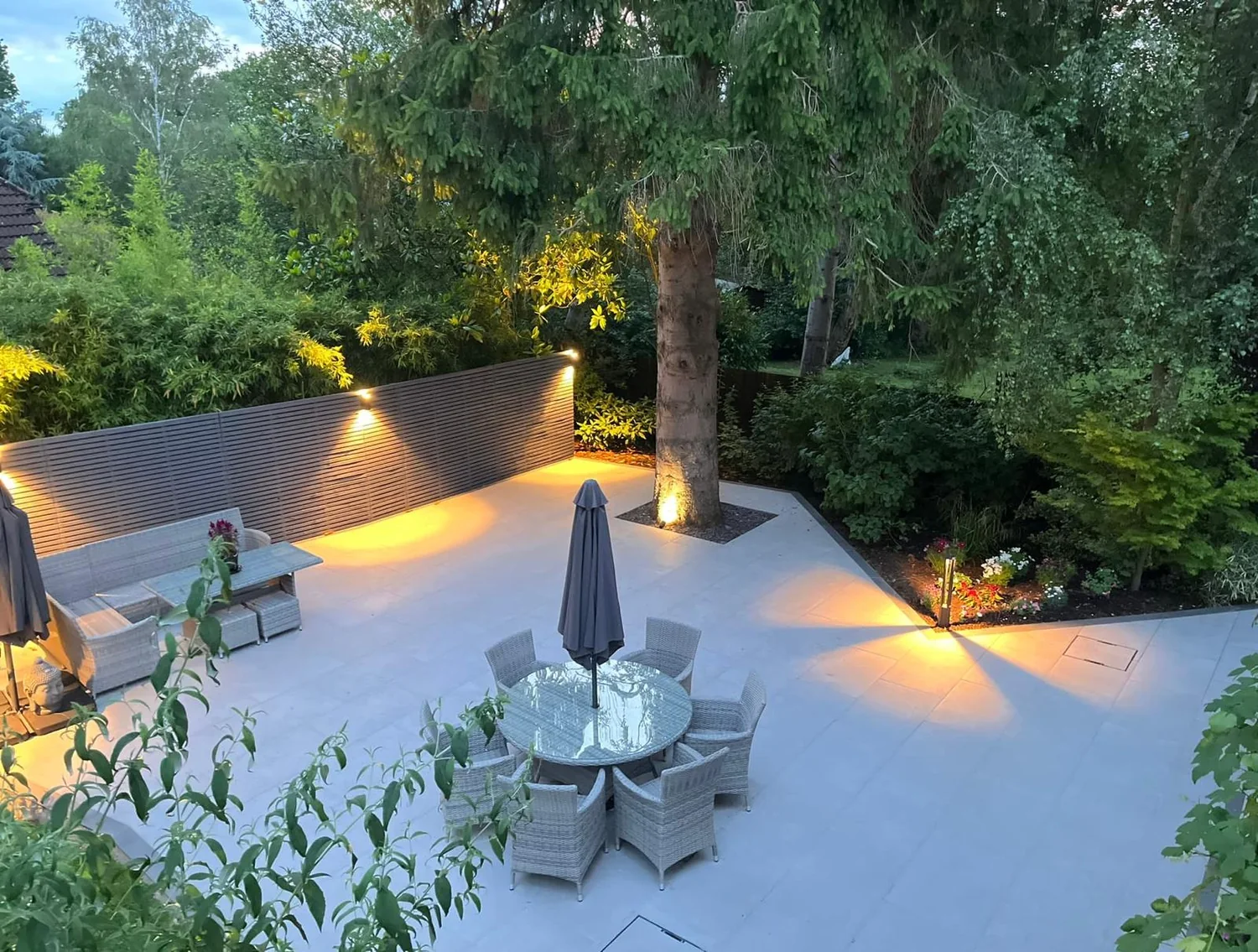 Porcelain terrace at dusk with garden lighting, a slatted screen and outdoor furniture