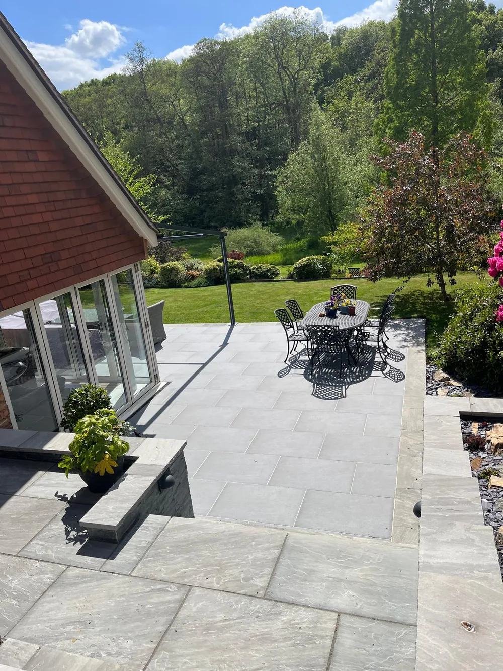 Porcelain terrace and dining table outside a conservatory looking down a mature garden