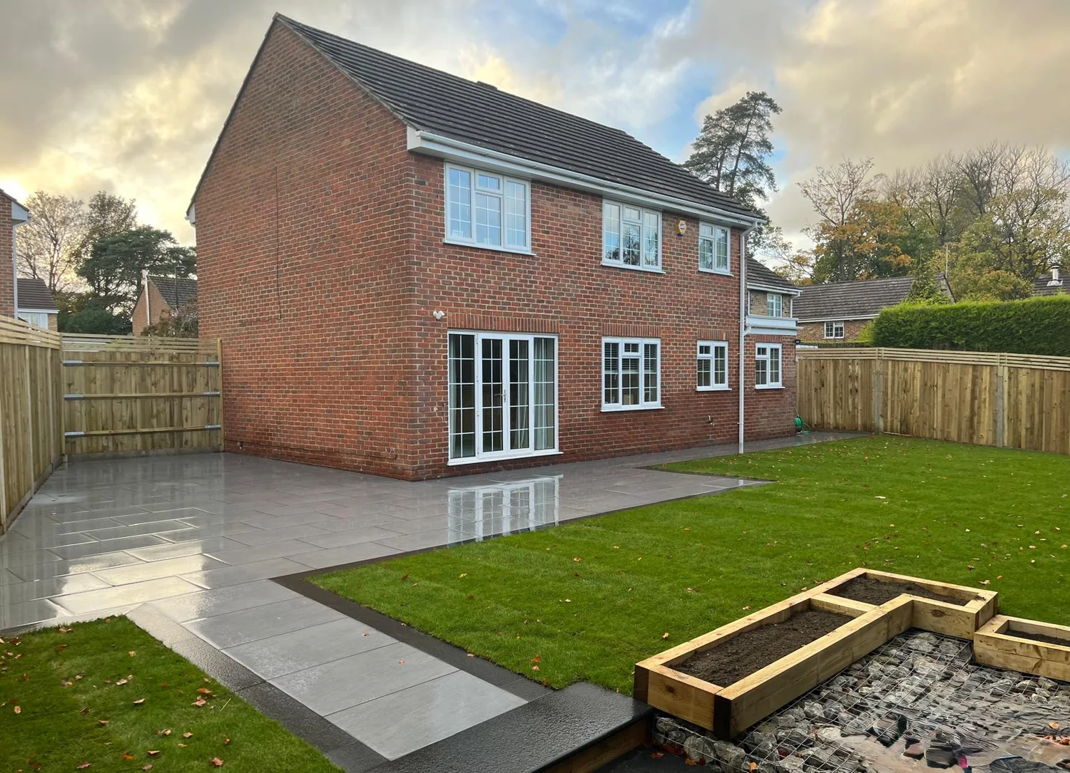 Large grey porcelain terrace with sleeper raised beds and a new lawn behind a detached house