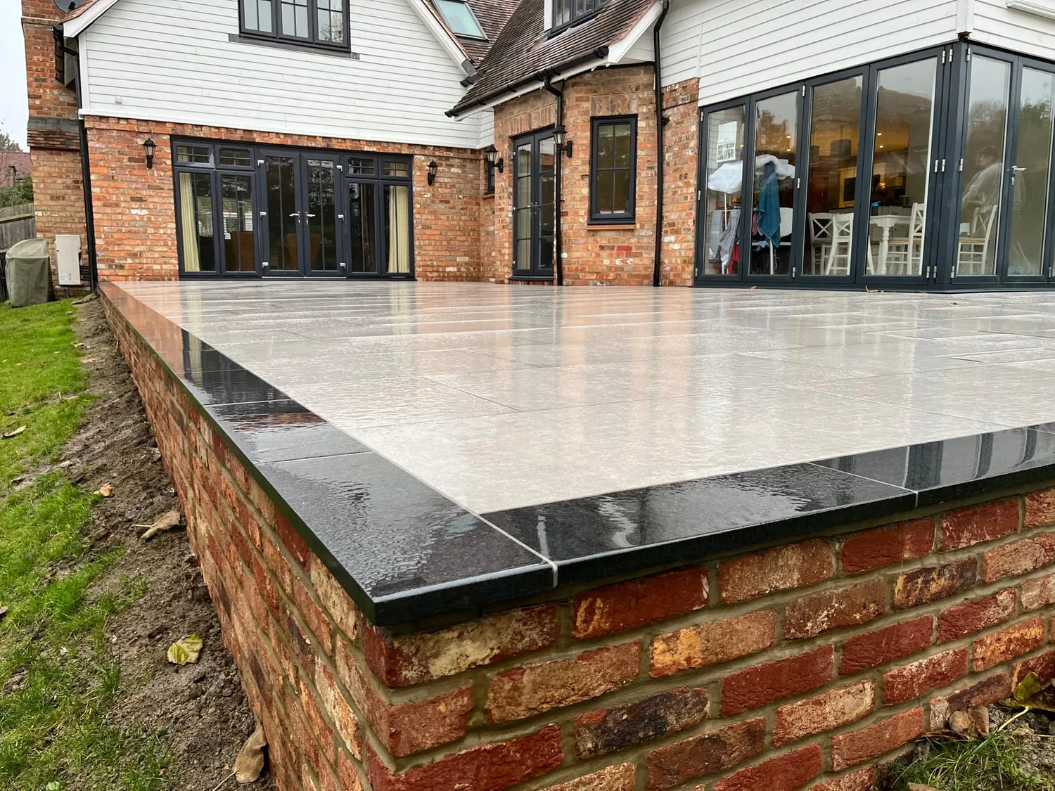Raised porcelain terrace with a dark edge detail on a brick retaining wall above the lawn