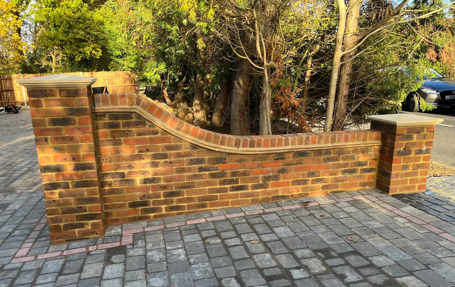 Curved red brick front wall with capped piers beside a grey block paved driveway