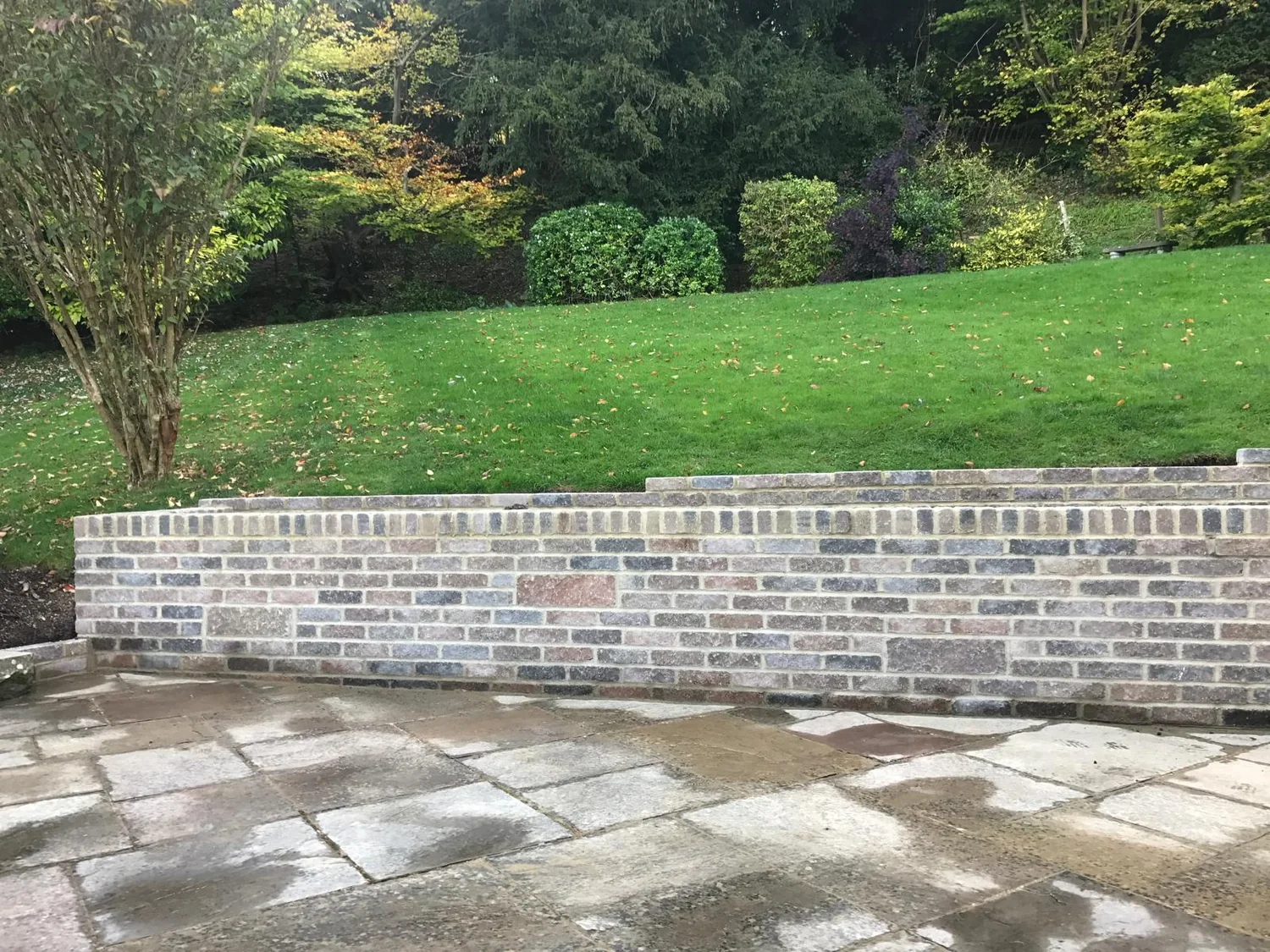 Reclaimed brick garden wall built along the top of a sandstone patio below a sloping lawn
