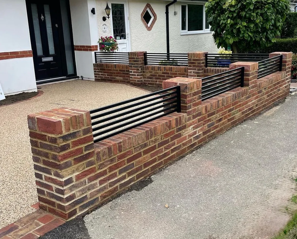 Brick front wall with black slatted panels beside a resin-bound driveway at a white rendered house